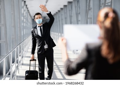 Businessman In Face Mask Waving To Assistance With Placard, Meeting In Airport. Middle-aged Entrepreneur With Suitcase Arrived For Business Meeting, Greeting Business Partner Or Representative