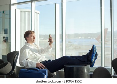 Businessman In Fifties Relaxing With Legs Up At Airport Terminal While Using Smartphone