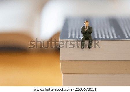 a businessman figure sitting on the books. Image of lifelong study, education.