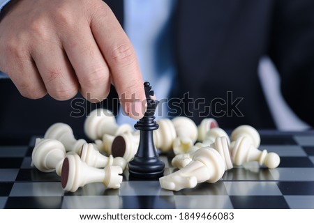 Businessman finger hands control chess king to success position on competition business game with falling enemy chess, meaning of planning and strategy decision and achievement goal concept.