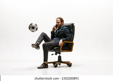 Businessman With Football Ball In Office. Soccer Freestyle. Concept Of Balance And Agility In Business. Manager Perfoming Tricks While Sitting On Chair And Speaking On The Smartphone Isolated On White