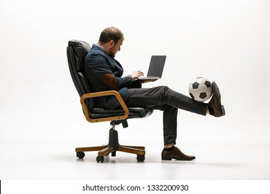 Businessman With Football Ball In Office. Soccer Freestyle. Concept Of Balance And Agility In Business. Manager Perfoming Tricks Sitting On Chair And Working On Laptop Isolated On White Studio