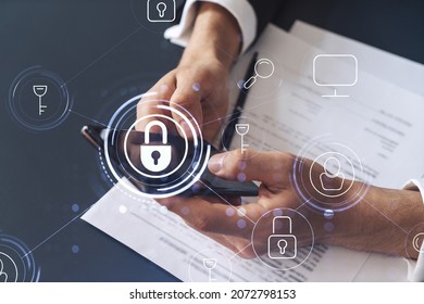 A businessman in formal wear reading the contract to prevent probability of risks in cyber security and checking details in the phone. Padlock Hologram icons over the working desk.