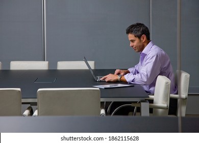 A businessman in formal wear with rolled up sleeves working alone on a laptop till late in the conference room