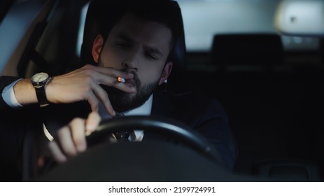 Businessman In Formal Wear Smoking Cigarette And Driving Car At Late Night