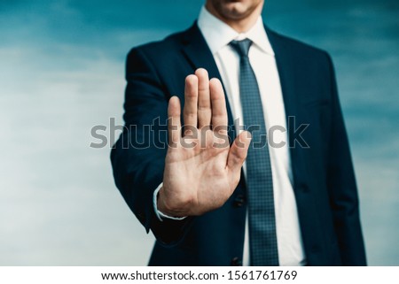 Businessman gesture. Male palm close-up in a gesture of stop. In the background a man in a blue suit with a tie.