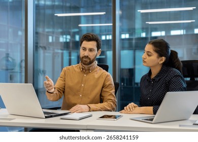 A businessman gestures while explaining something to a businesswoman at a modern office.
