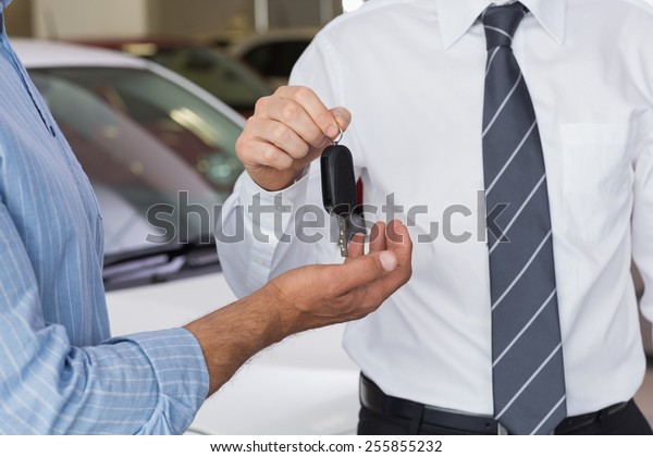 Businessman giving car key to customer at new\
car showroom