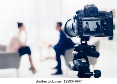 Businessman Giving Interview To Journalist In Office, Camera On Tripod On Foreground