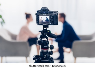 Businessman Giving Interview To Journalist In Office, Camera On Tripod On Foreground