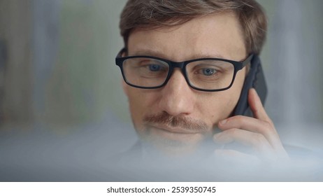 Businessman with glasses speaking on the phone, partially obscured by blurred laptop. Front view and close up portrait - Powered by Shutterstock