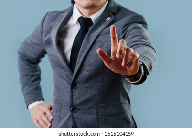 Businessman in a gray suit is making objection gesture by extending hand with the index finger up, holding his second hand on the waist over blue background. Cropped, no head. - Shutterstock ID 1515104159