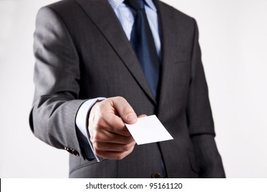 Businessman in grey suit and a blue shirt with a blue tie, shows business card with copy space, shallow dept of field, isolated on a grey background - Shutterstock ID 95161120
