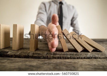 Businessman halting the domino effect inserting his hand between falling and upright wooden blocks in a close up conceptual image.