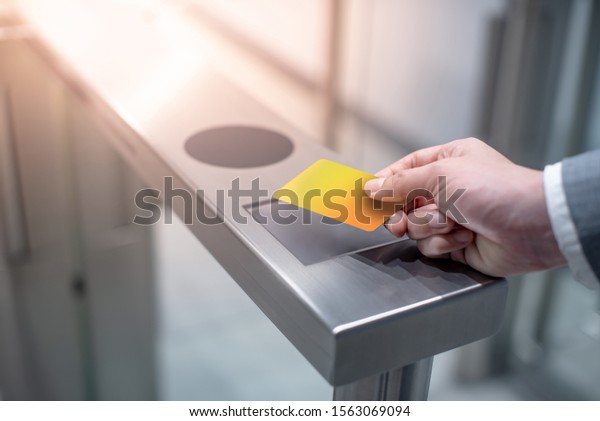 Businessman hand with business wear using yellow\
smart card to open automatic gate machine in office building.\
Working routine\
concept