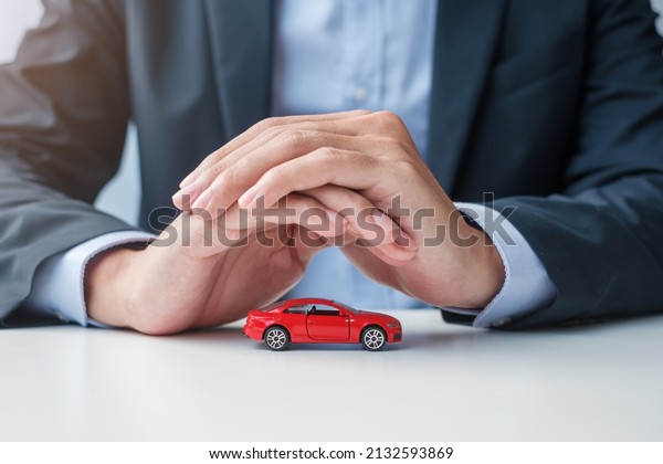 Businessman hand cover or protection red car toy\
on table. Car insurance, warranty, repair, Financial, banking and\
money concept