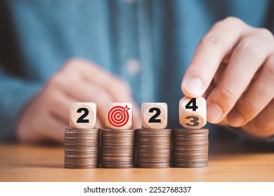 Businessman hand flipping wooden block cube from 2023 to 2024 on coins stacking for setup objective target business cost and budget planing of new year concept. - Shutterstock ID 2252768337