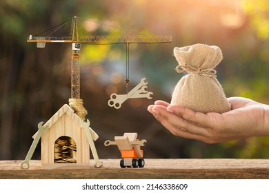 Businessman hand hold money bag and the home and coin with growing interest value and tower crane with money in the public park, Loan for business investment with construction the real estate concept. - Shutterstock ID 2146338609