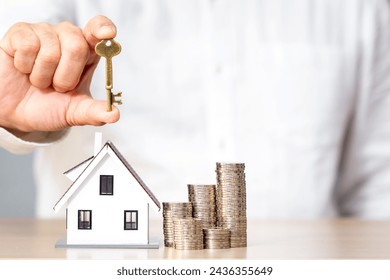 Businessman hand holding the house key and the home model and stack gold coin with growing interest put on the desk in the in the office, Loan and ownership of real estate concept. - Powered by Shutterstock