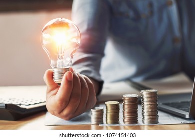 Businessman Hand Holding Lightbulb With Saving Money In Office. Concept Accounting And Energy