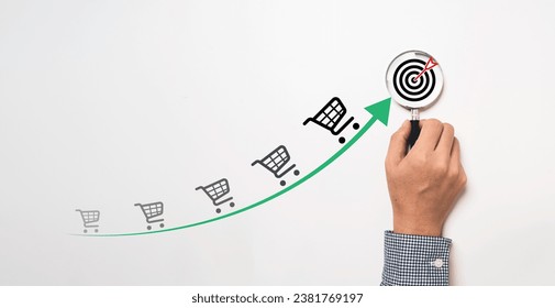 Businessman hand holding magnifier glass with target board , increasing arrow trend graph of sale volume and bigger shopping trolley cart for  online sale business growth until achieve goal concept. - Powered by Shutterstock