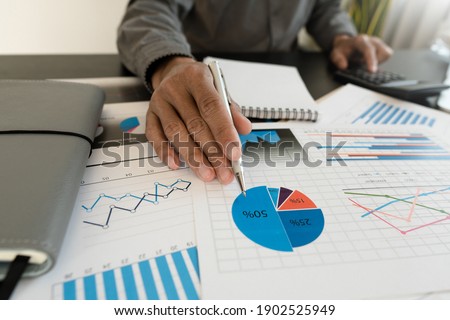 Businessman hand holding pen and pointing at financial paperwork with financial network diagram.