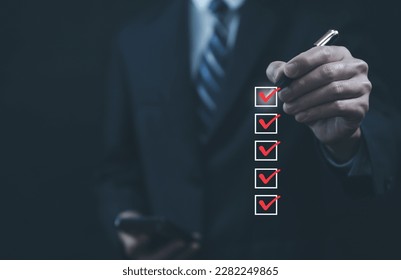Businessman hand holding a pen ticking a red checkmark on a box in the list Show on the virtual screen. Checklist Ideas in Business Survey items and questionnaires. copy space - Shutterstock ID 2282249865
