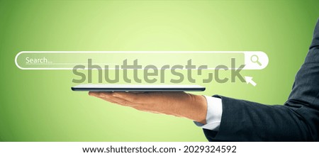 Businessman hand holding tablet with creative website search bar hologram on green background. Internet and browse concept