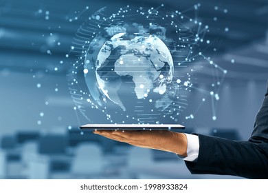 Businessman hand holding tablet with glowing globe interface on blurry office background. Global futuristic innovation concept. Double exposure - Shutterstock ID 1998933824