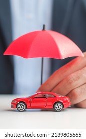 Businessman Hand Holding Umbrella And Cover  Red Car Toy On Table. Car Insurance, Warranty, Repair, Financial, Banking And Money Concept