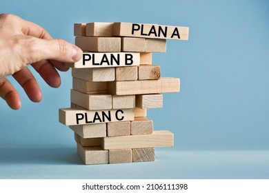 Businessman hand holding Wooden block Plan B. Wooden tower with words PLAN A, PlAN B, PLAN C on light blue background with copy space. Business strategy, failure analysis. Business concept