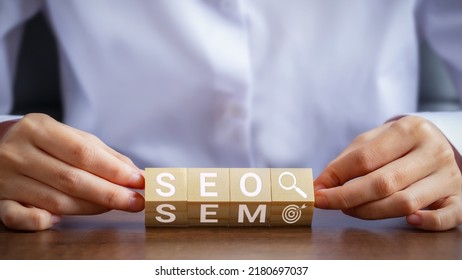 Businessman hand holding wooden block with letters SEO and SEM. Concepts about managing search engine based and targeted marketing.