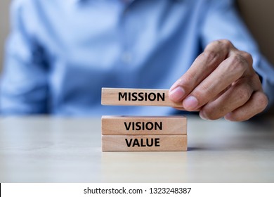 Businessman hand holding wooden building blocks with MISSION, VISION, CORE VALUE Concepts