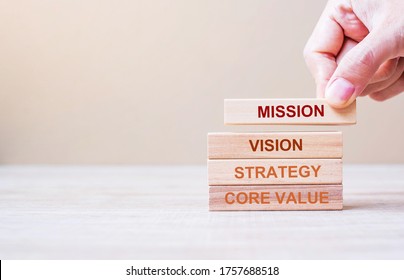 Businessman hand holding wooden building blocks with MISSION, VISION, CORE VALUE and STRATEGY word. Business concepts