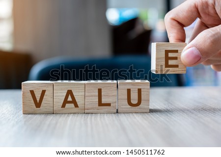 Businessman hand holding wooden cube block with Value business word on table background. Mission, Vision and core values concept