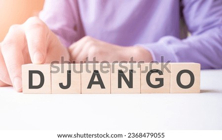 Businessman hand holding wooden cube block with DJANGO business word on table background.