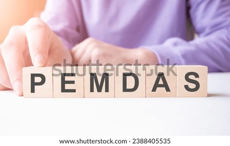 Businessman hand holding wooden cube block with PEMDAS business word on table background.