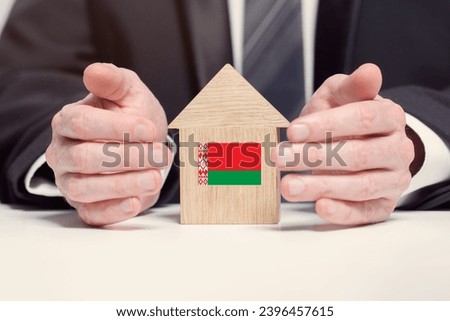Businessman hand holding wooden home model with Belorussian flag. insurance and property concepts