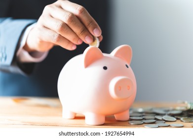 businessman hand inserting a coin into a piggy bank for business and save money