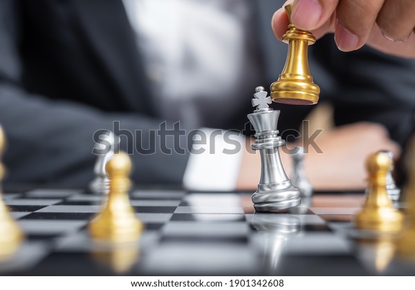 businessman hand moving gold Chess King figure\
and Checkmate enermy or opponent during chessboard competition.\
Strategy, Success, management, business planning, interruption and\
leadership concept