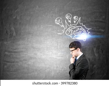 Businessman with hand on chin standing at blackboard, brain and bulbs over his head. Concept of new idea.