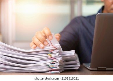 Businessman hand pick up Stack overload documents report paper with colorful paperclip with fair light to analyze data, business and paperless concept.