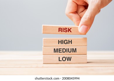 Businessman Hand Placing Or Pulling Wooden Block With Risk Text Over High Medium And Low. Planning, Risk Management, Economic, Finance And Corporate Concepts