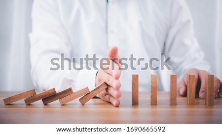 Businessman hand stop falling down of wood block .planing and strategy business disruption concept.