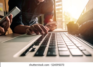 Businessman hand using laptop and tablet with social network diagram and two colleagues discussing data on desk as concept in morning light.