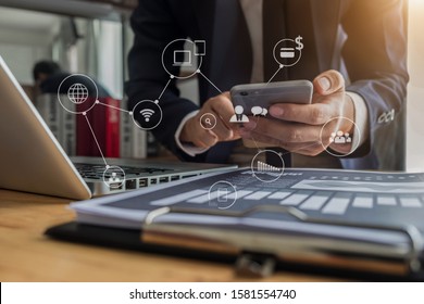 Businessman hand working digital marketing media in virtual screen with mobile phone and modern compute with VR icon diagram at office in morning light. 