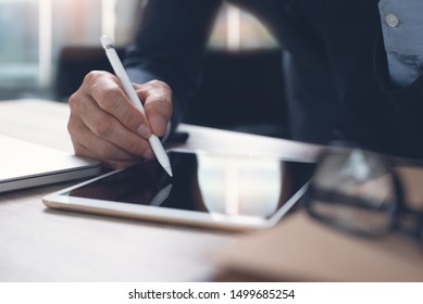 Businessman hand working with stylus pen on digital tablet with laptop computer in modern office, close up. Business man signing contract on tablet pc via mobile apps. electronic signature concept