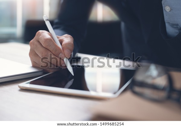 Businessman hand working with stylus pen on\
digital tablet with laptop computer in modern office, close up.\
Business man signing contract on tablet pc via mobile apps.\
electronic signature\
concept