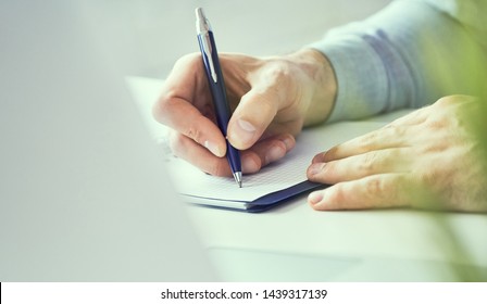 Businessman Hand Writing Note On A Notebook Close-up. Business Man Working At Office Desk. Close Up Of Empty Notebook On A Blackboard With Office Supplies.