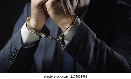 Empresario con esposas arrestado por fraude financiero, sentado en la sala de interrogatorios